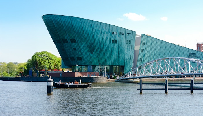 NEMO Science Museum exterior with canal and pedestrian bridge in Amsterdam.