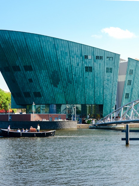 NEMO Science Museum exterior with canal and pedestrian bridge in Amsterdam.