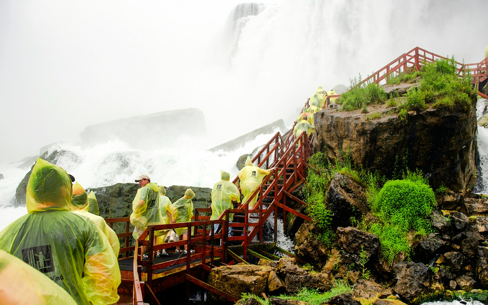Visitors in raincoats on wooden platform at Cave of the Winds, Niagara Falls.