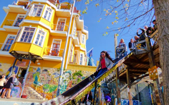Woman sliding down a colorful slide in Valparaíso, Chile, near vibrant murals and a yellow building.