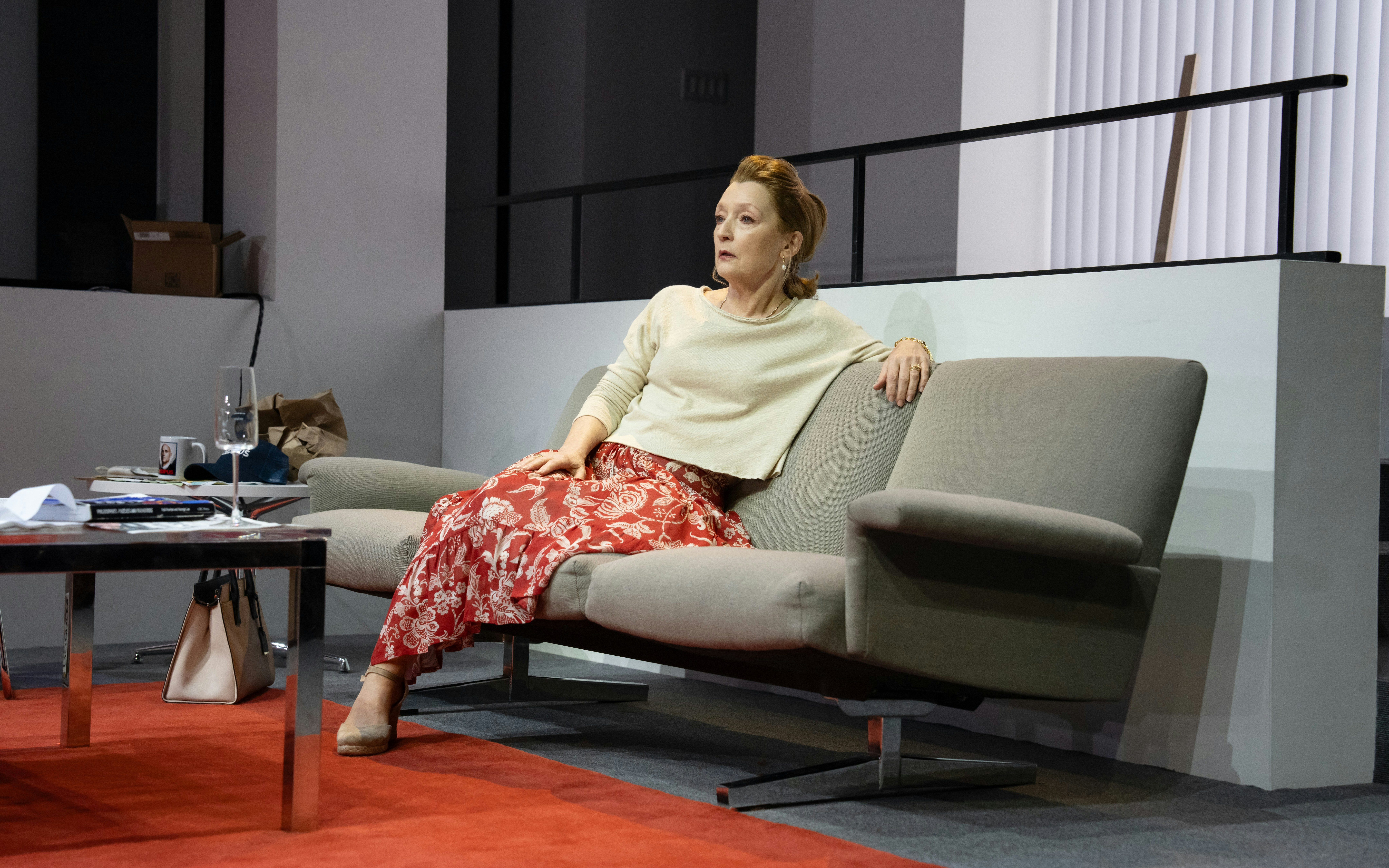 Stage scene from Oedipus Broadway show with actor seated on a modern sofa.