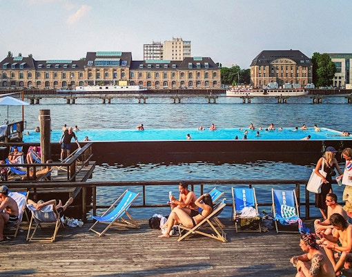 Badeschiff Berlin floating pool on River Spree with city skyline in background.