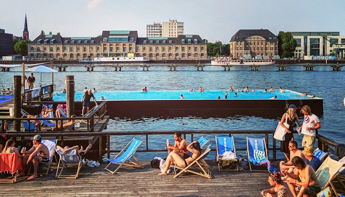Badeschiff Berlin floating pool on River Spree with city skyline in background.