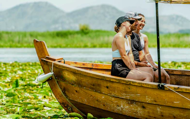 Tourists enjoying a wooden boat ride on Lake Skadar with mountains in the background.