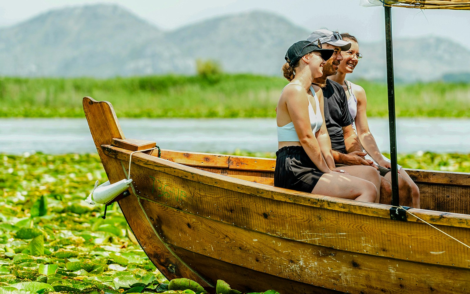 Tourists enjoying a wooden boat ride on Lake Skadar with mountains in the background.