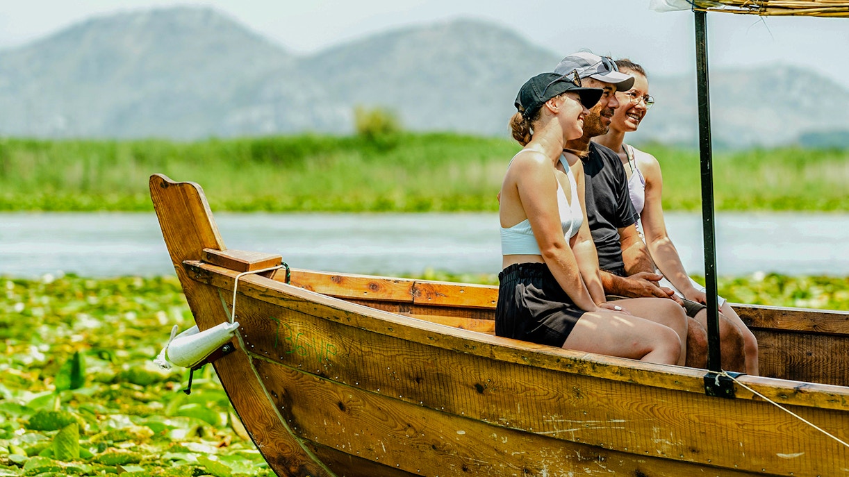 Tourists enjoying a wooden boat ride on Lake Skadar with mountains in the background.