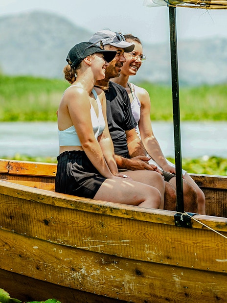 Tourists enjoying a wooden boat ride on Lake Skadar with mountains in the background.
