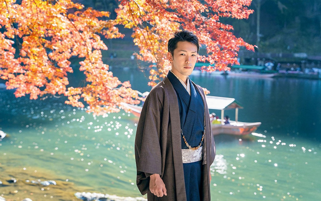 Man in kimono by river with autumn leaves in Kyoto Arashiyama.
