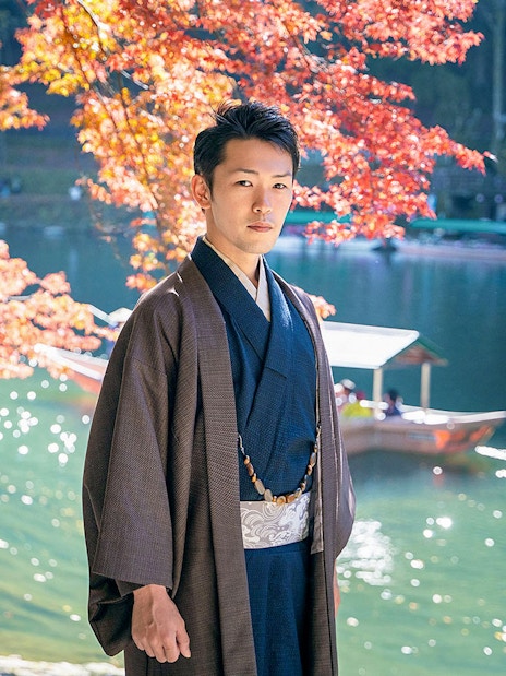 Man in kimono by river with autumn leaves in Kyoto Arashiyama.