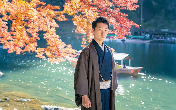 Man in kimono by river with autumn leaves in Kyoto Arashiyama.