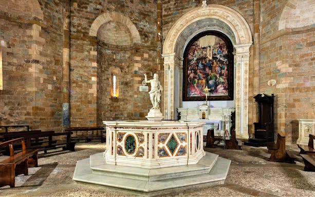 Volterra Cathedral interior with ornate baptistry and religious artwork.