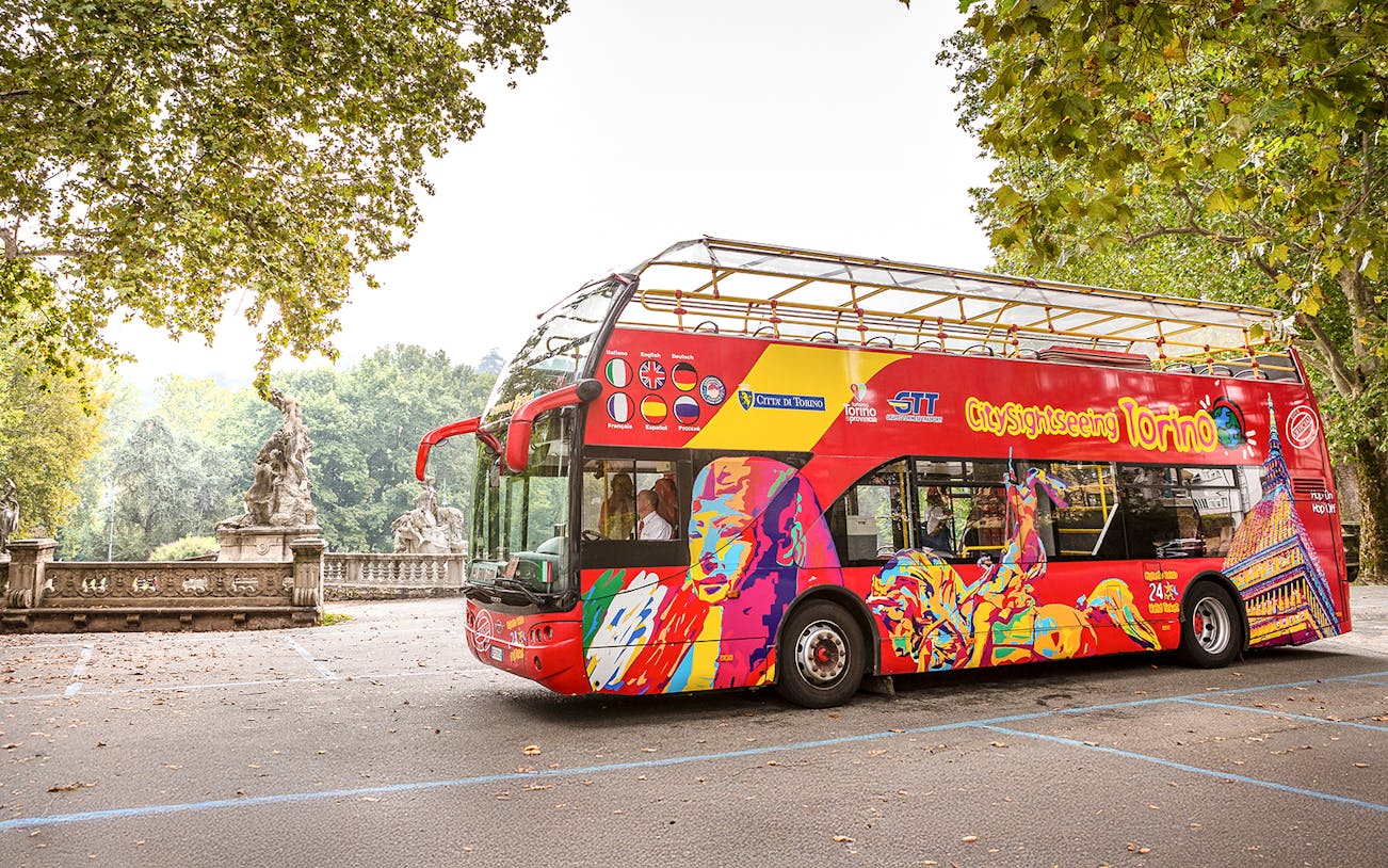 City Sightseeing hop on hop off bus in Turin near historic statues.