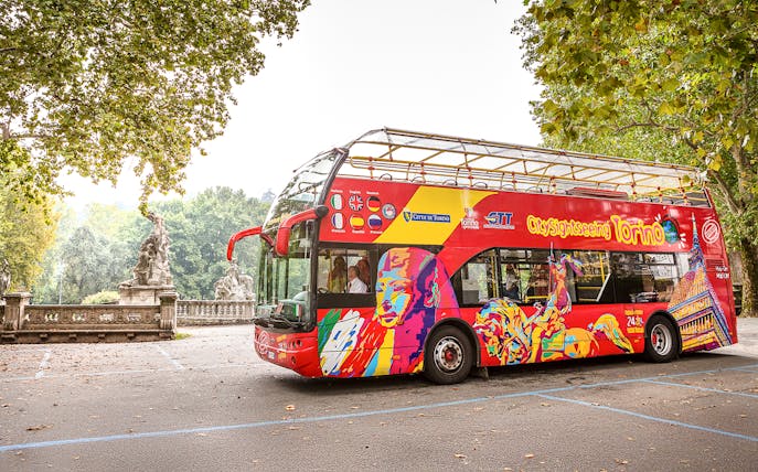 City Sightseeing hop on hop off bus in Turin near historic statues.