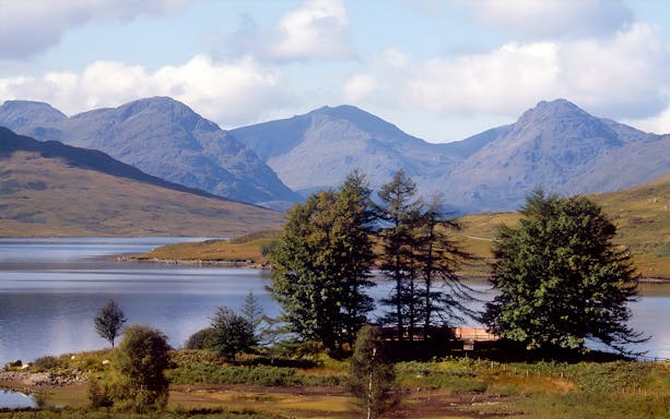 Loch Lomond with surrounding hills and trees, part of the day tour from Edinburgh.