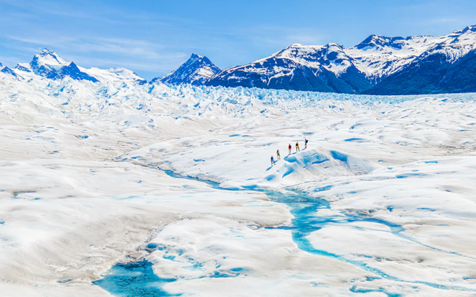 Tourists hiking on Perito Moreno Glacier, Argentina, with snowy peaks in the background.