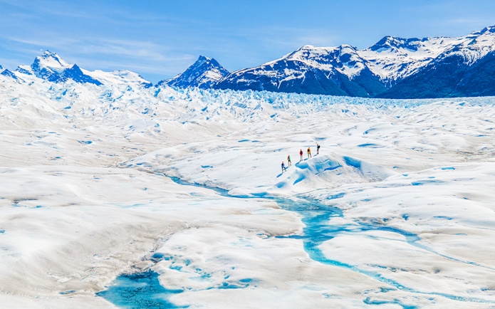 Tourists hiking on Perito Moreno Glacier, Argentina, with snowy peaks in the background.