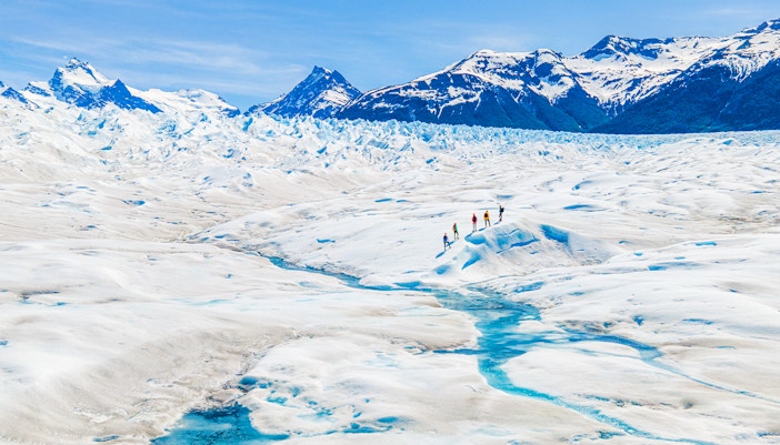 Tourists hiking on Perito Moreno Glacier, Argentina, with snowy peaks in the background.