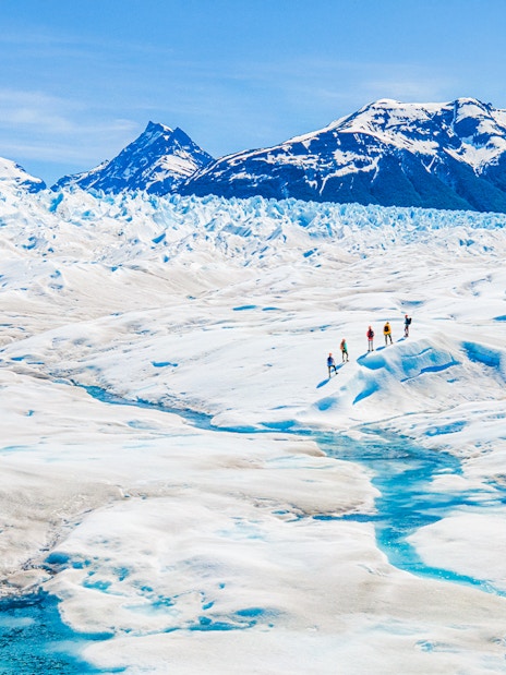 Tourists hiking on Perito Moreno Glacier, Argentina, with snowy peaks in the background.