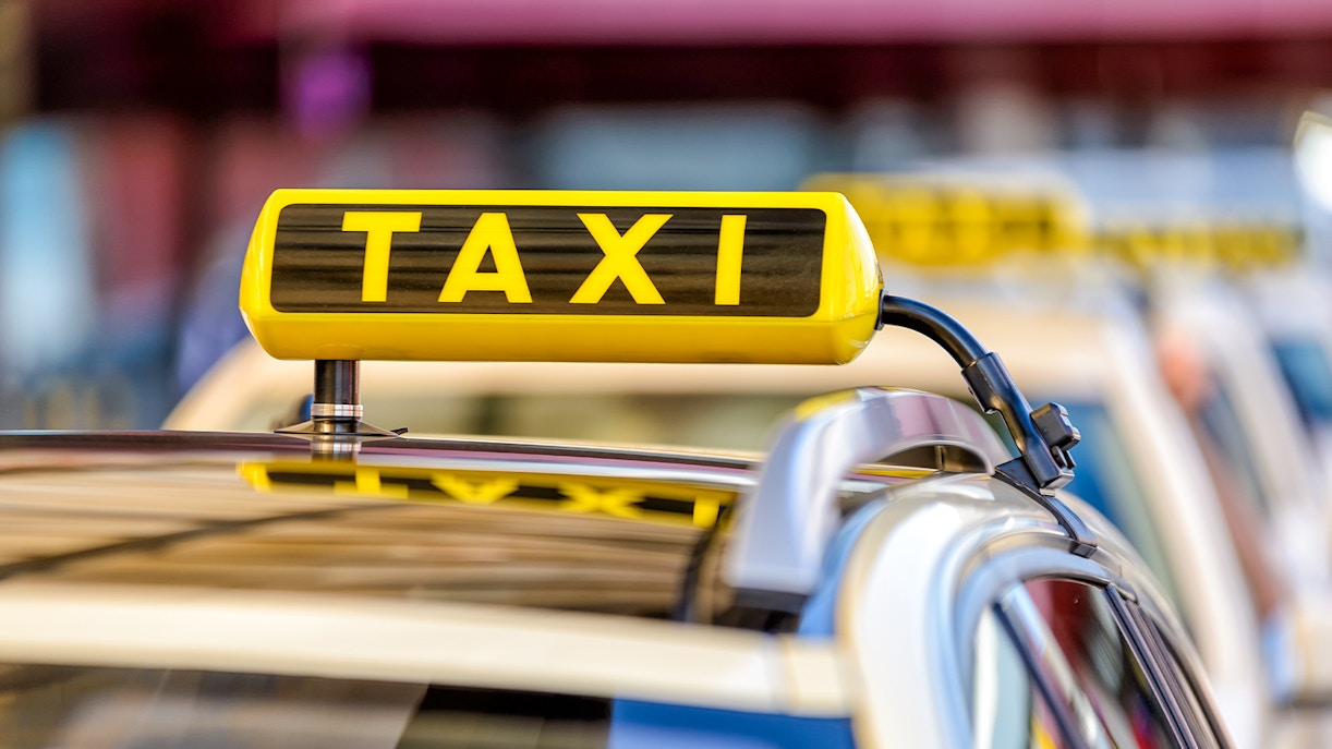 Yellow taxi sign on car roof in urban setting.