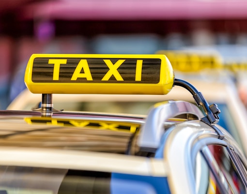 Yellow taxi driving through Times Square, New York City, with bright billboards and bustling crowds.