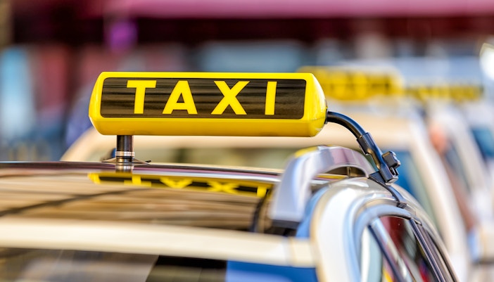 Yellow taxi driving through Times Square, New York City, with bright billboards and bustling crowds.
