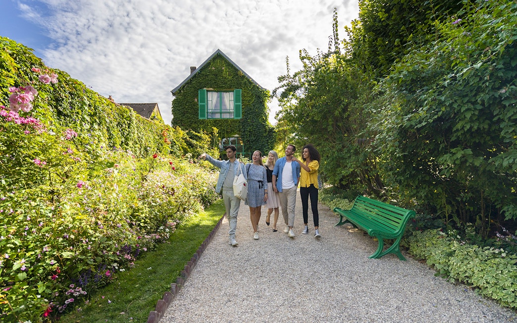 Visitors exploring Giverny Garden with a guide, surrounded by lush greenery and flowers.