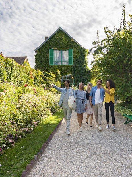 Visitors exploring Giverny Garden with a guide, surrounded by lush greenery and flowers.