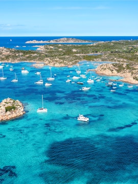 Boats anchored in the turquoise waters of La Maddalena, Sardinia, with rocky islands in the background.