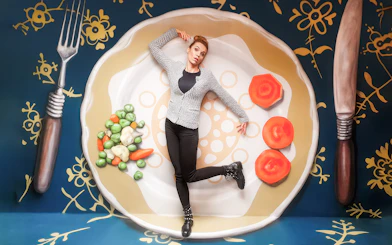 Person posing on oversized plate with vegetables at Museum of Fantastic Illusions.
