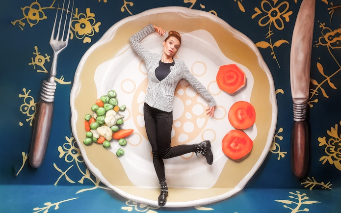 Person posing on oversized plate with vegetables at Museum of Fantastic Illusions.