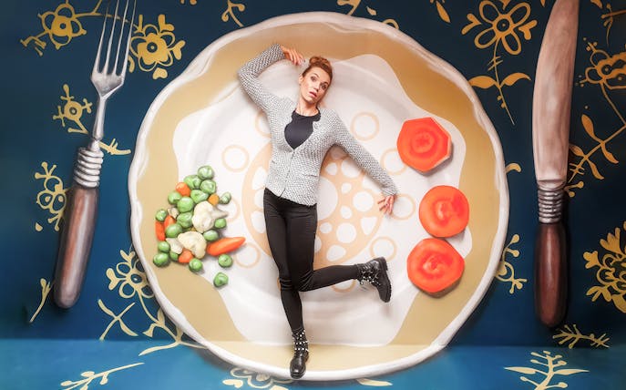 Person posing on oversized plate with vegetables at Museum of Fantastic Illusions.