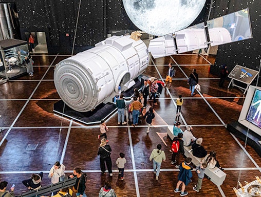 Visitors exploring space exhibit at Science & Industry Museum, Paris, featuring a large satellite model.