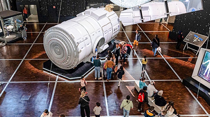 Visitors exploring space exhibit at Science & Industry Museum, Paris, featuring a large satellite model.