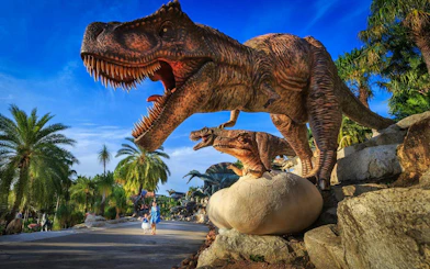 Dinosaurs at Nong Nooch Tropical Garden, Thailand, with palm trees and visitors.