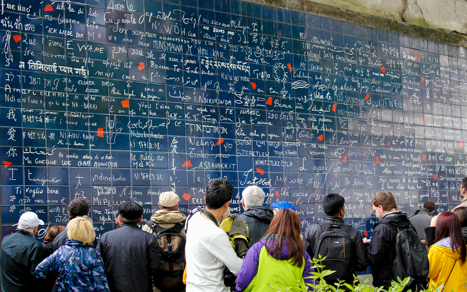 Visitors viewing the Wall of Love in Montmartre, Paris, with "I love you" in multiple languages.