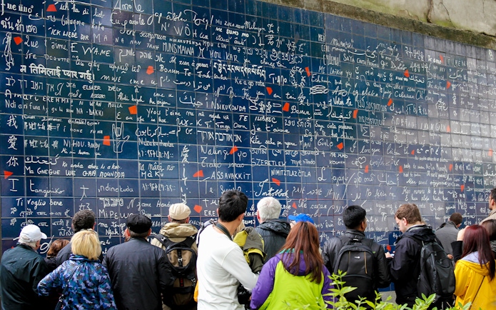 Visitors viewing the Wall of Love in Montmartre, Paris, with "I love you" in multiple languages.