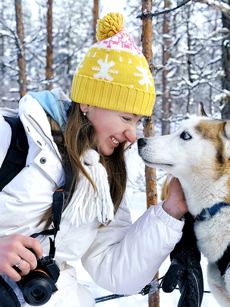 Woman interacting with a husky in snowy Rovaniemi forest during sledding experience.