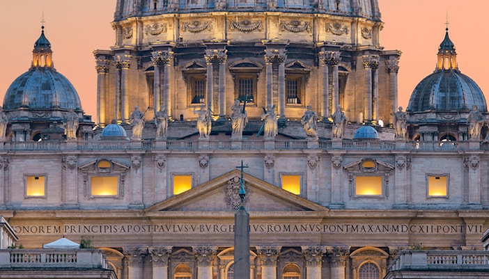 St. Peter's Basilica illuminated at dusk with vibrant sky in Rome.