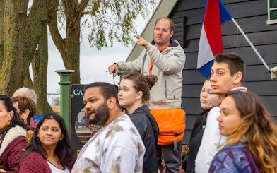 Tour guide leading visitors at Keukenhof with Dutch flag in background.