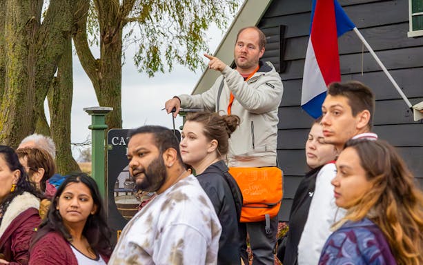 Tour guide leading visitors at Keukenhof with Dutch flag in background.