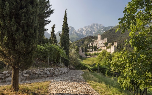 Avio Castle surrounded by trees and mountains in Trentino, Italy.