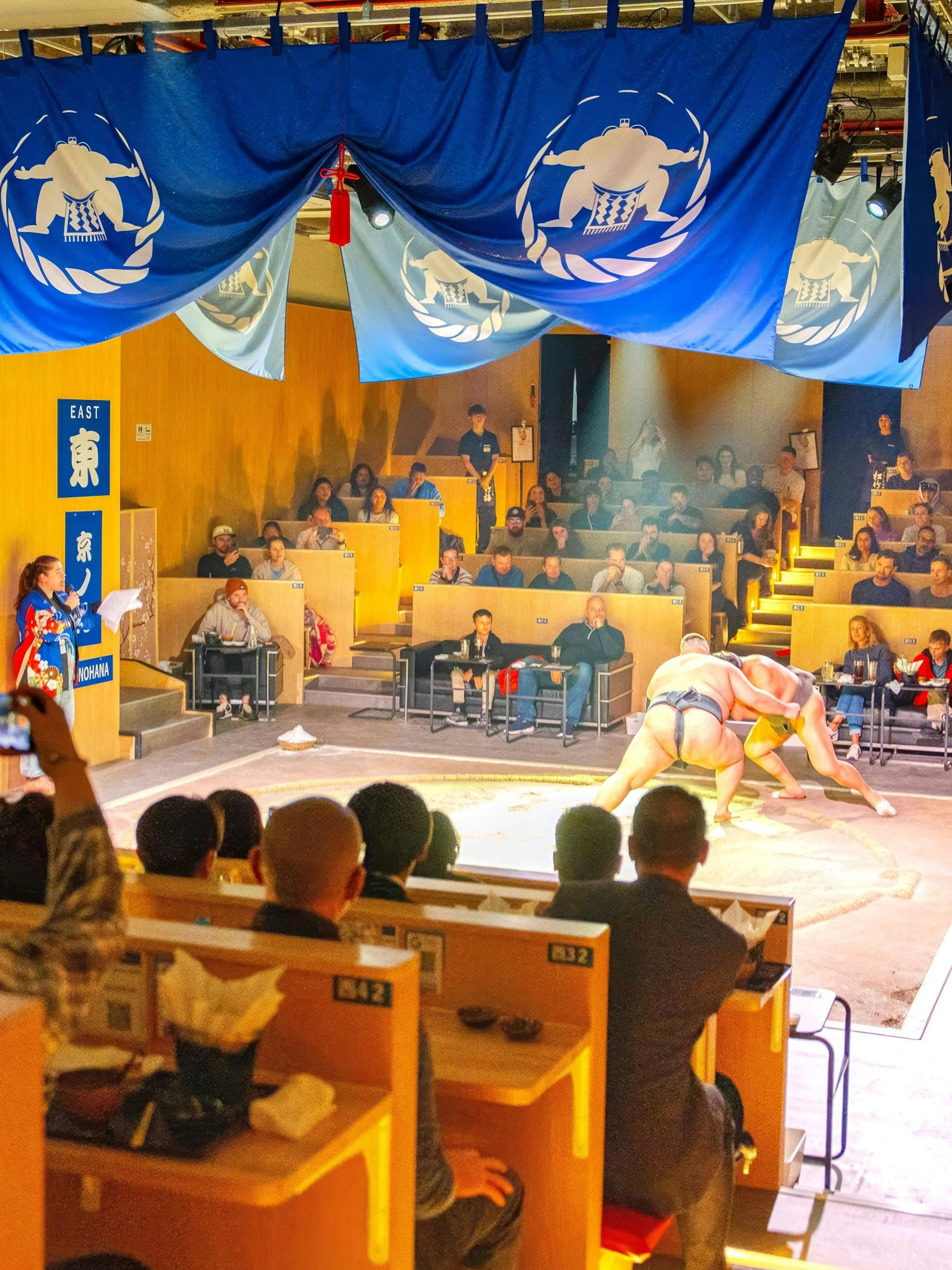 Sumo wrestlers performing in a Kyoto arena with audience enjoying the show.