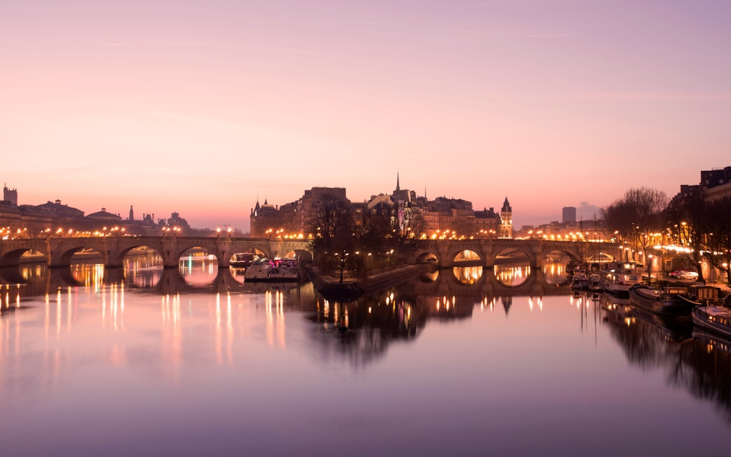 Paris evening skyline with illuminated bridge over the Seine River.