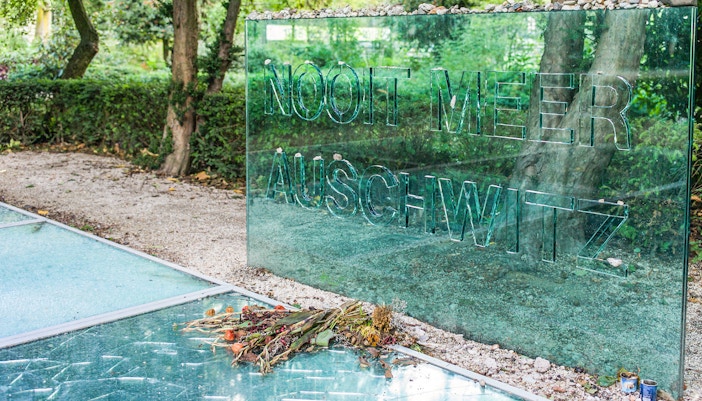 Auschwitz Memorial glass panel with stones and flowers in Amsterdam park.