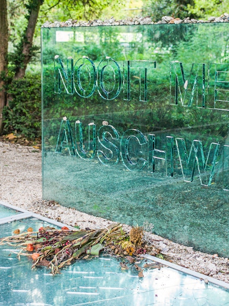 Auschwitz Memorial glass panel with stones and flowers in Amsterdam park.