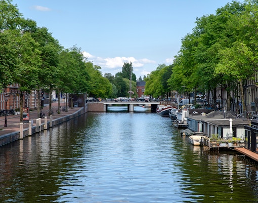 Amsterdam canal with houseboats and a bridge in the background.