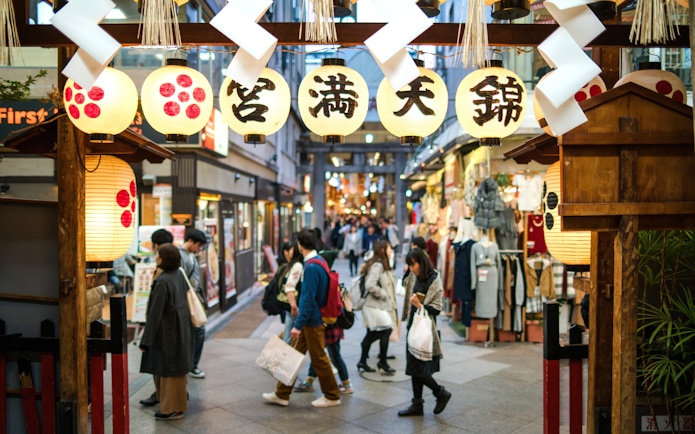 Shoppers walking through Nishiki Market in Kyoto, Japan, under traditional lanterns.