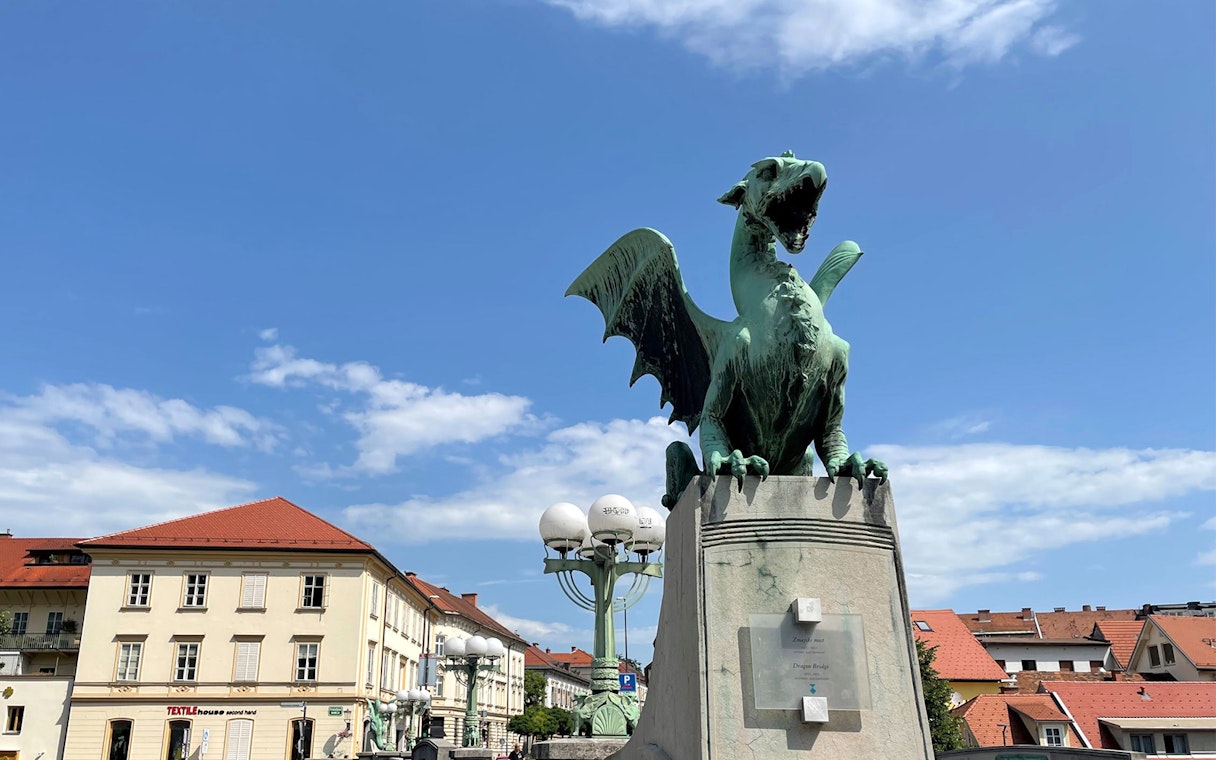 Dragon statue on Dragon Bridge in Ljubljana, Slovenia, with city buildings in the background.