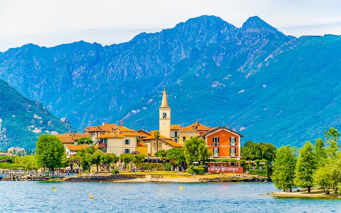 Island village with church tower and colorful buildings on Isole Borromee, Italy, viewed from the water.