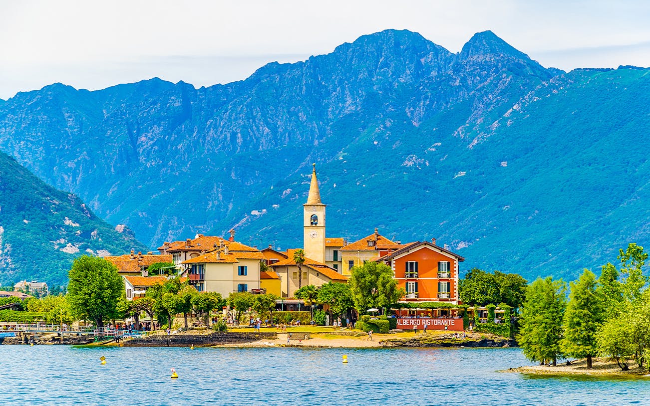 Island village with church tower and colorful buildings on Isole Borromee, Italy, viewed from the water.
